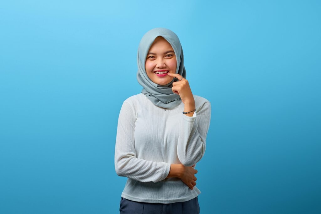 Cheerful teenage girl wearing hijab, posing in front of a bright blue backdrop.