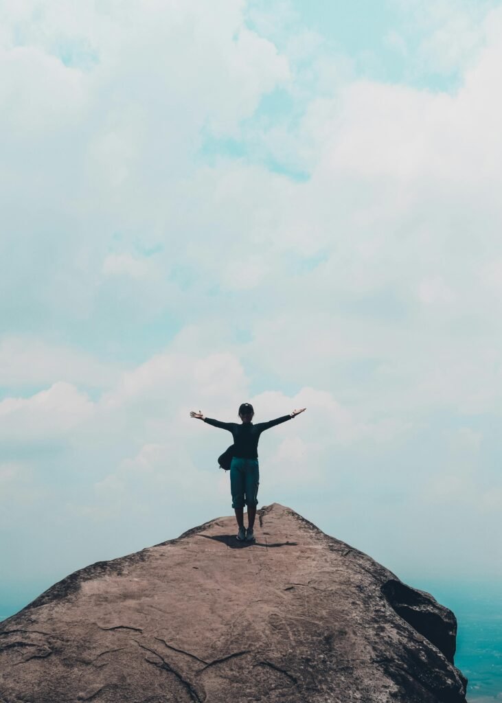 A woman standing with arms wide on a mountain peak, embracing the sky.